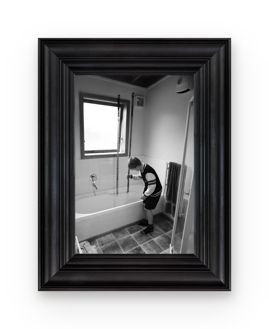 A boy measuring a bath with a tape in black and white, in a deep black frame.