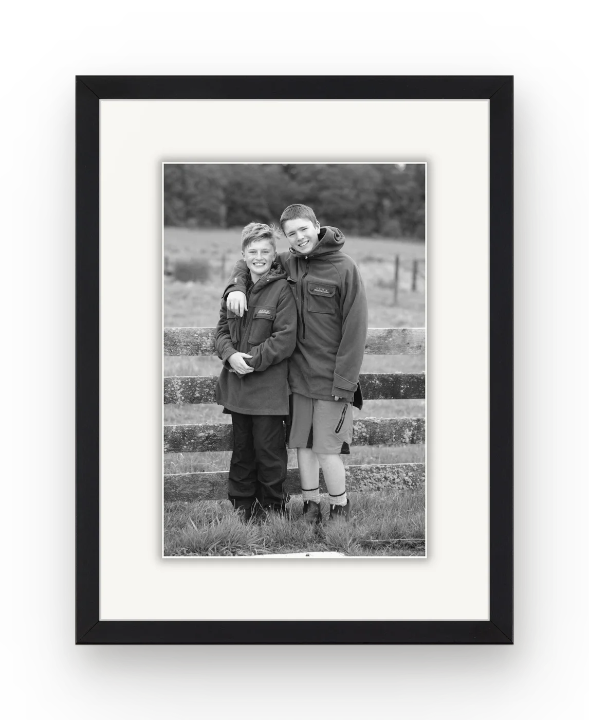Two brothers in front of a farm fence in black and white, framed in black with a white mat.