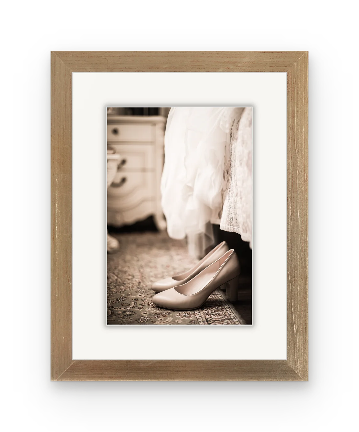 Wedding shoes beside the hem of a white dress, in an antique gold frame with a white mat.