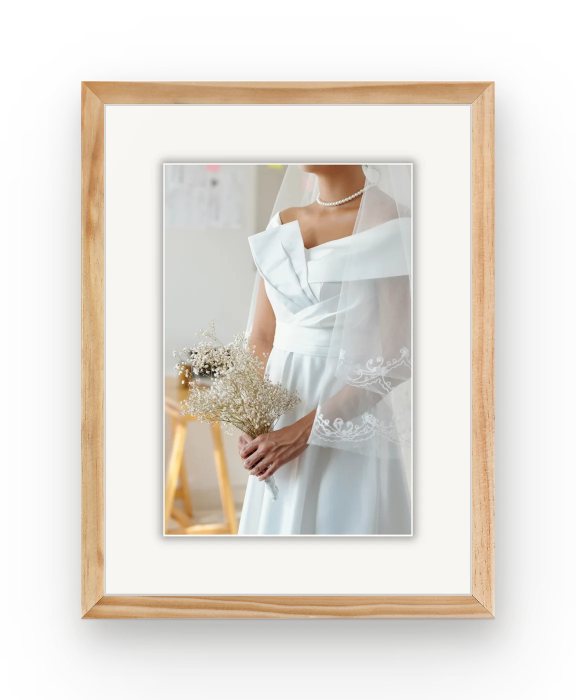 A bride in a veil holding a small bouquet, framed in natural wood with a white mat.